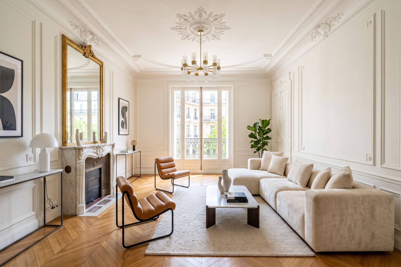 Grand salon lumineux de style classique avec parquet point de Hongrie, moulures blanches murales, cheminée surmontée d'un miroir doré et mobilier contemporain épuré.