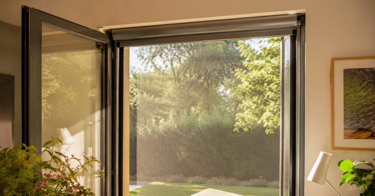 Moustiquaire enroulable grise installée sur une porte-fenêtre donnant sur un jardin